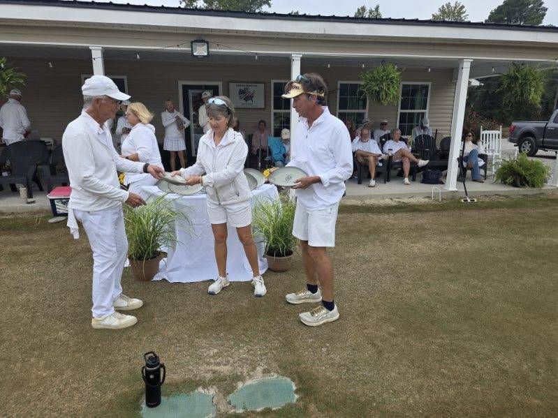 People in white clothing accepting awards outdoors on a grassy field.