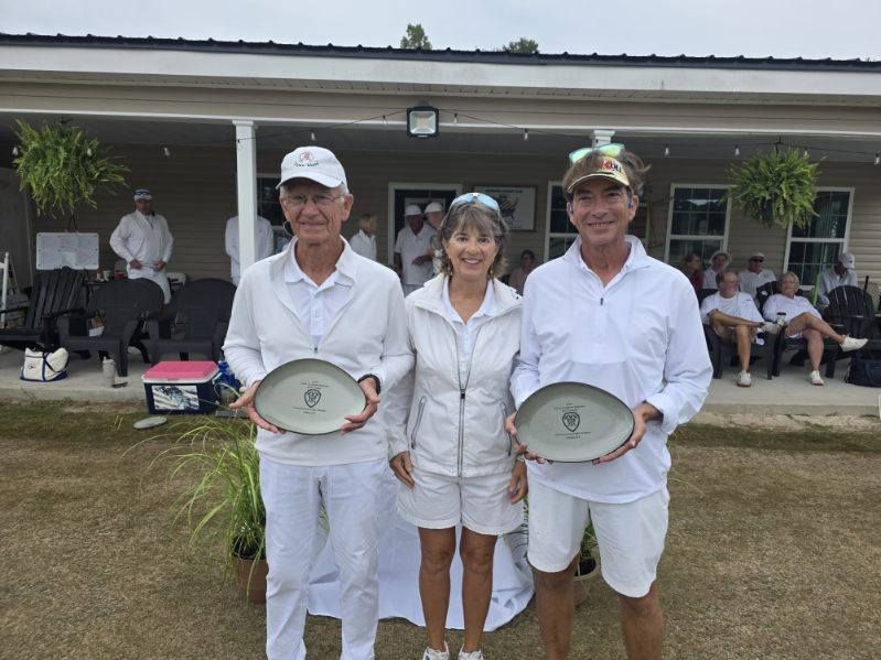 Three people in white holding plates, smiling, outdoors in front of a building.