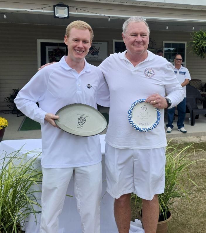 Two men in white outfits hold plates outside. One smiles; the other looks at the camera. A man in the background.