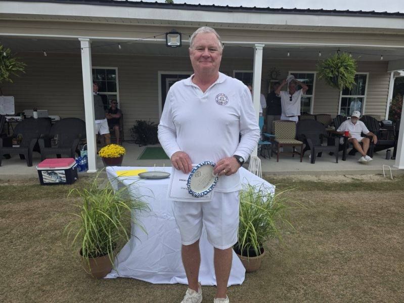 Man in white holding a prize, standing outside a building.