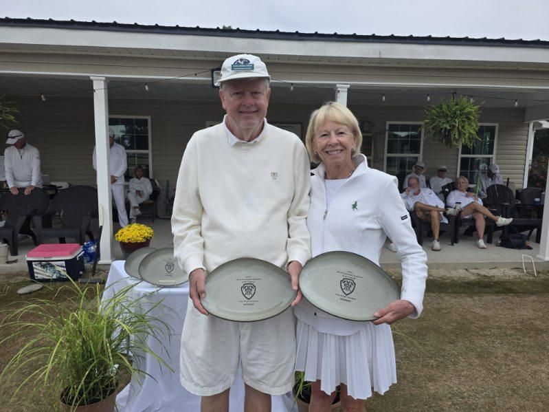 A man and woman holding plates, smiling. They are on a lawn in front of a building.