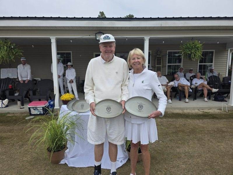 Two people holding plates outdoors, likely after a competition, with others watching in the background.