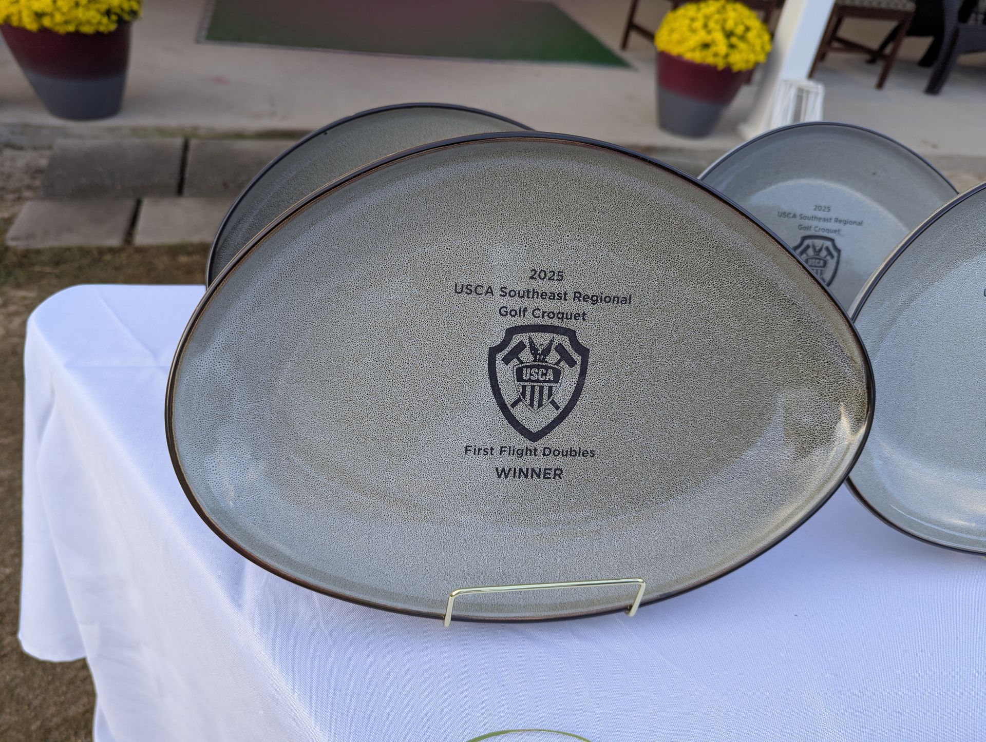 Football-shaped gray plates with black text and logo, on a white tablecloth, near potted yellow flowers.
