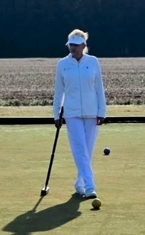 Woman in white playing croquet, holding mallet on a green lawn.
