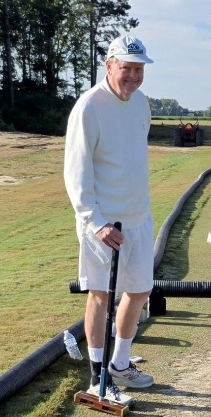 Man in white playing croquet outdoors, holding mallet, smiling.
