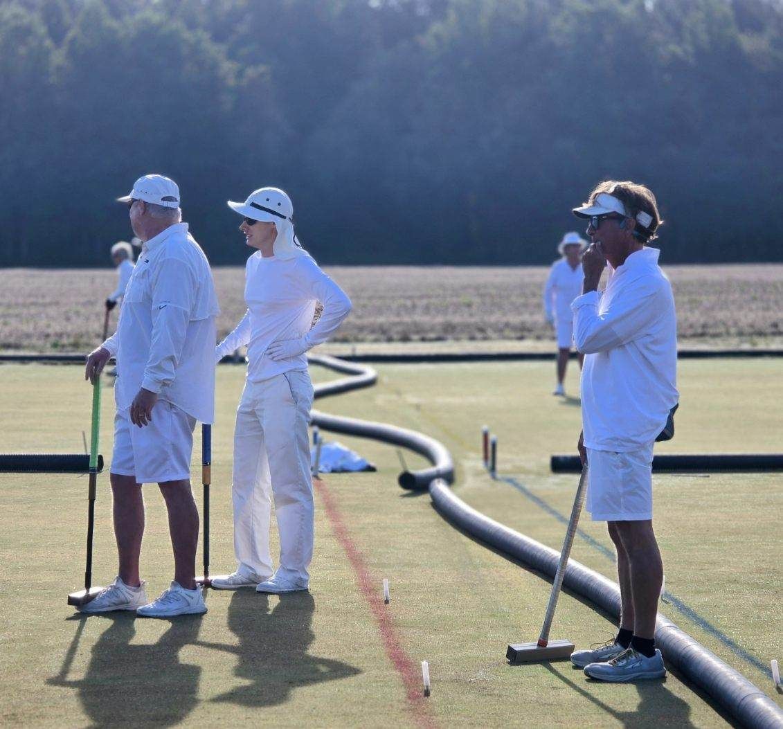 People in white attire playing croquet on a green field with mallets.
