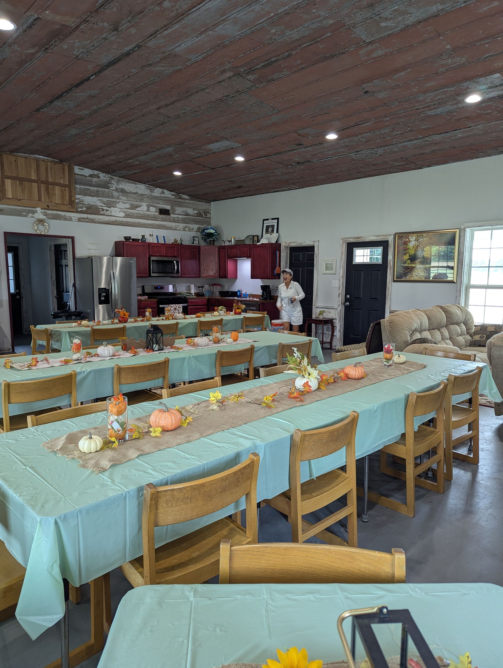 Long tables set for a gathering, decorated with fall centerpieces; rustic interior with red kitchen in background.