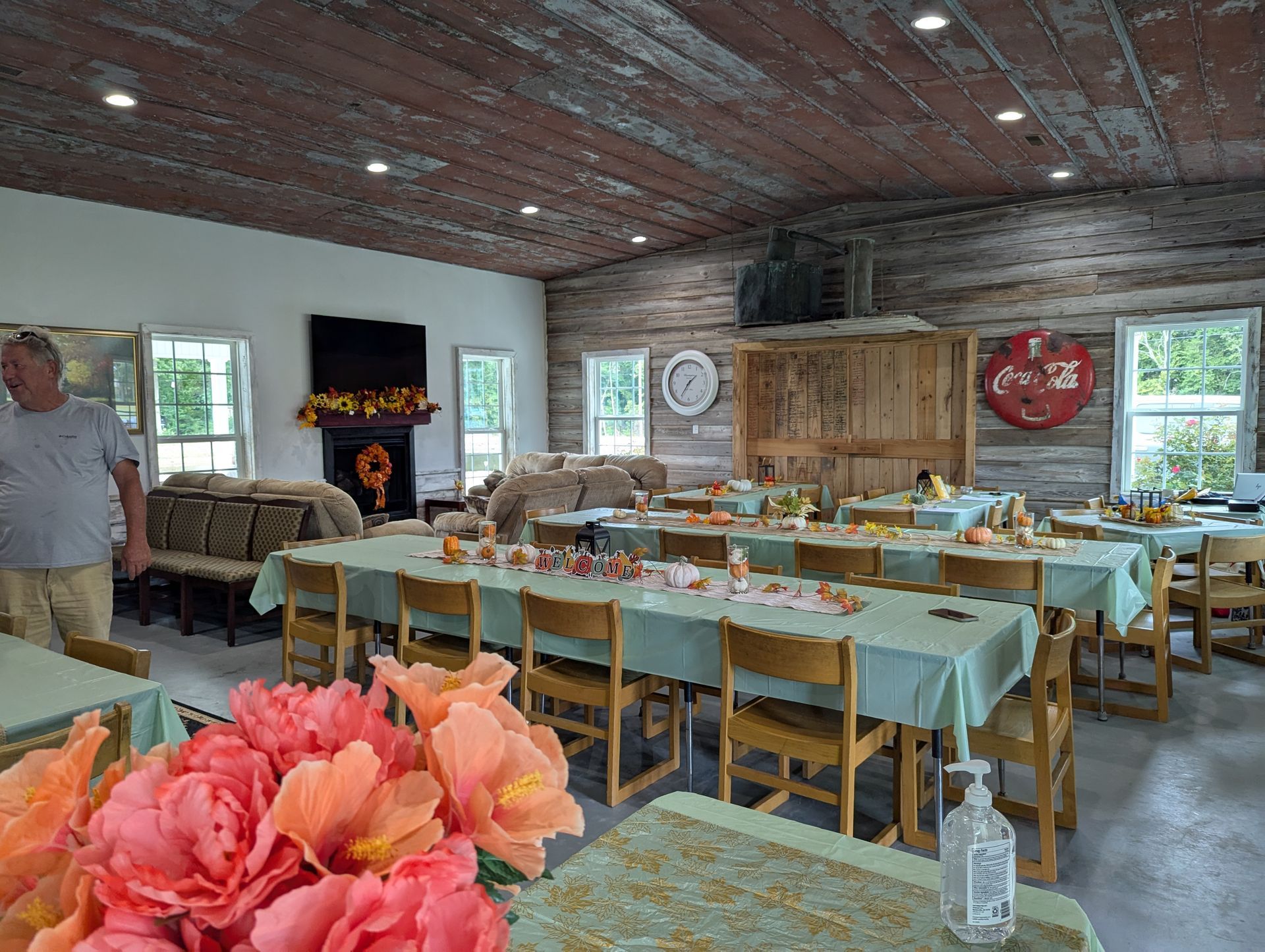 Event space with tables set for a meal. Decorations include pumpkins and flowers. Man stands near the entrance.