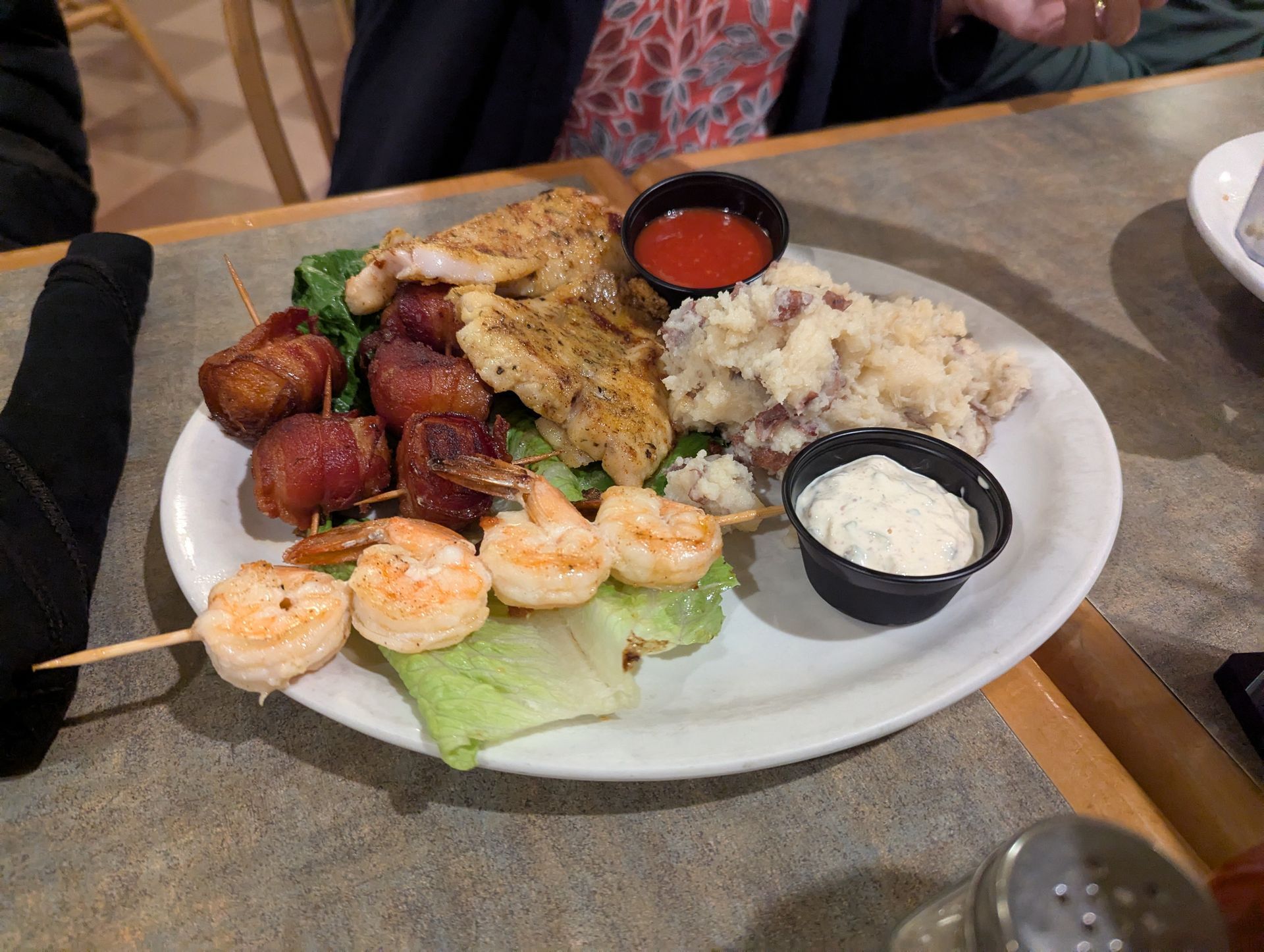 Plate of food: chicken, shrimp skewer, bacon-wrapped bites, mashed potatoes, and dipping sauces.
