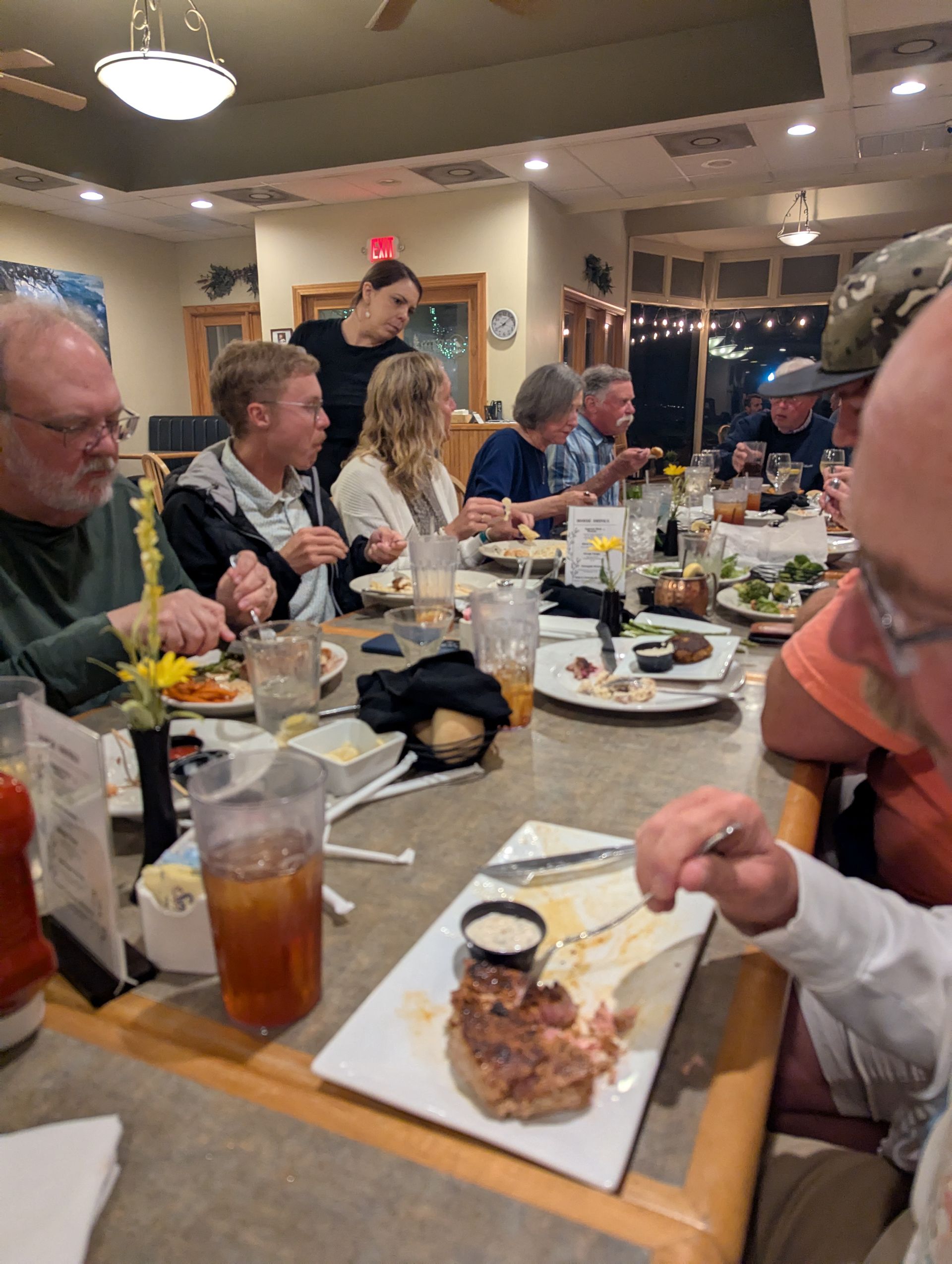 People seated around a long restaurant table, eating. A server stands nearby.