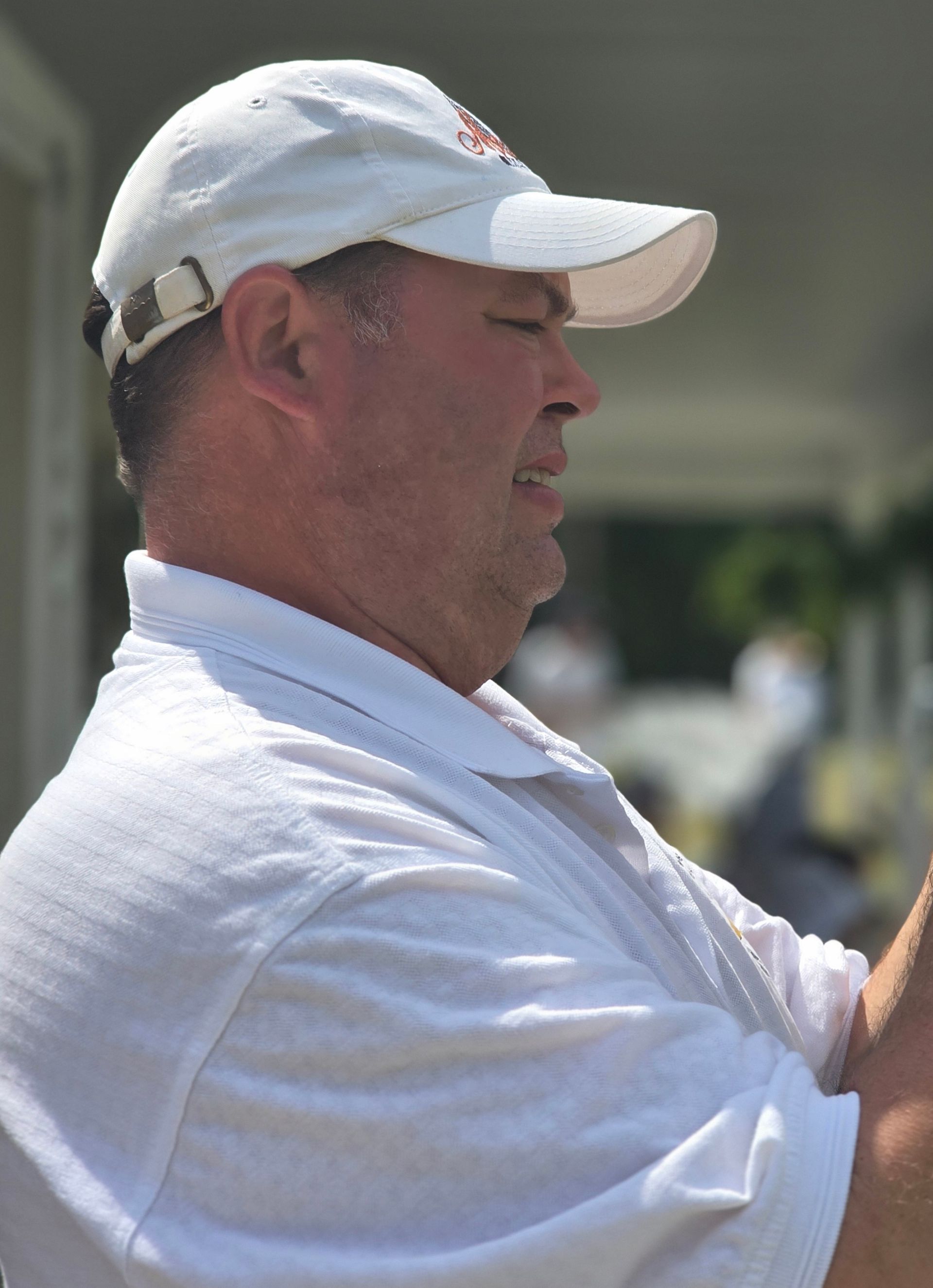 Man in white cap and polo shirt, side view, outdoors.