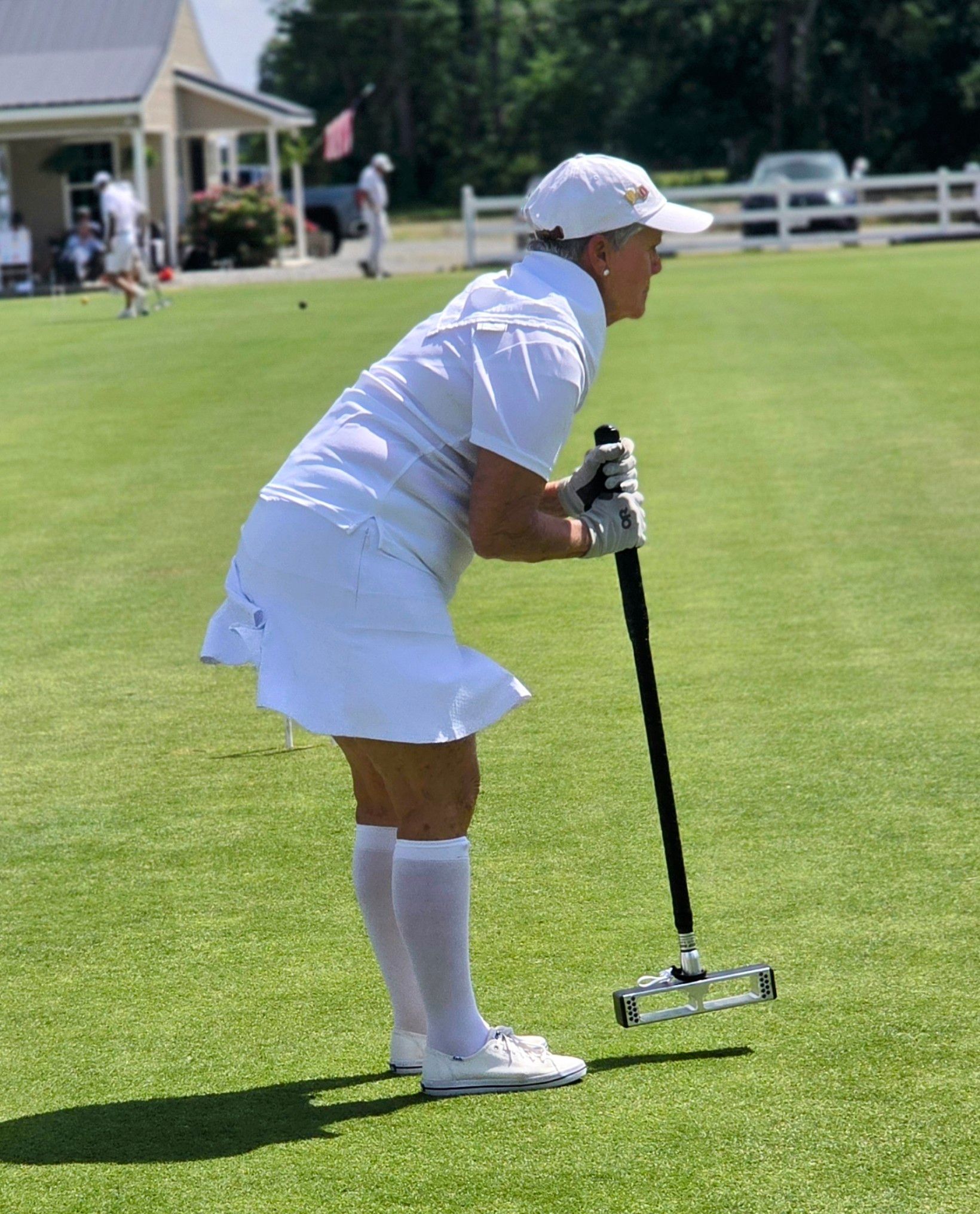 Woman in white outfit aiming a croquet mallet on a green lawn.