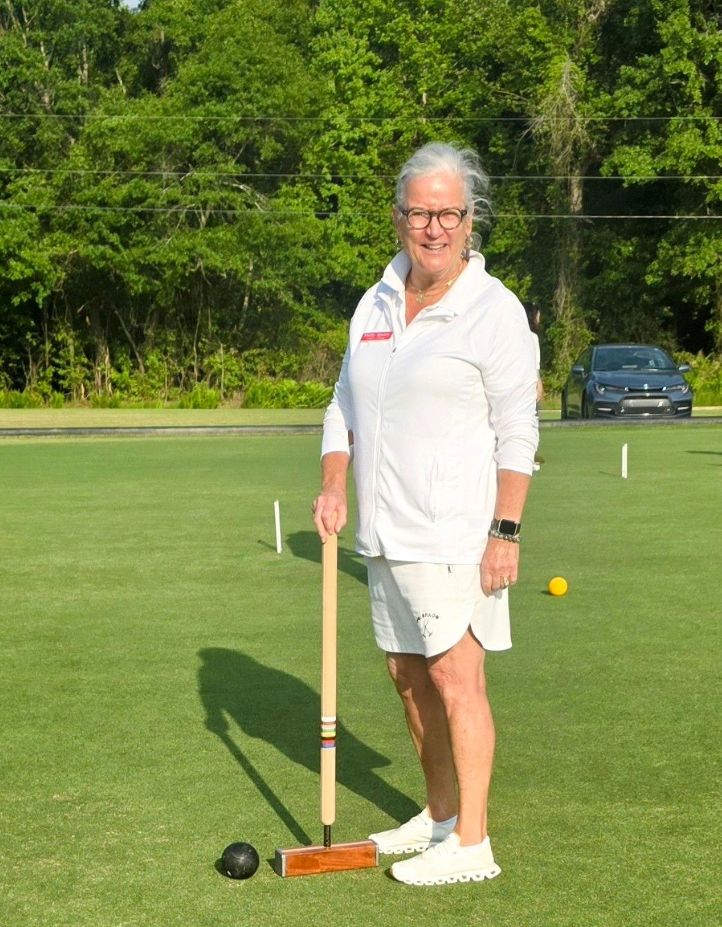 Woman in white playing croquet on a green lawn, holding mallet.