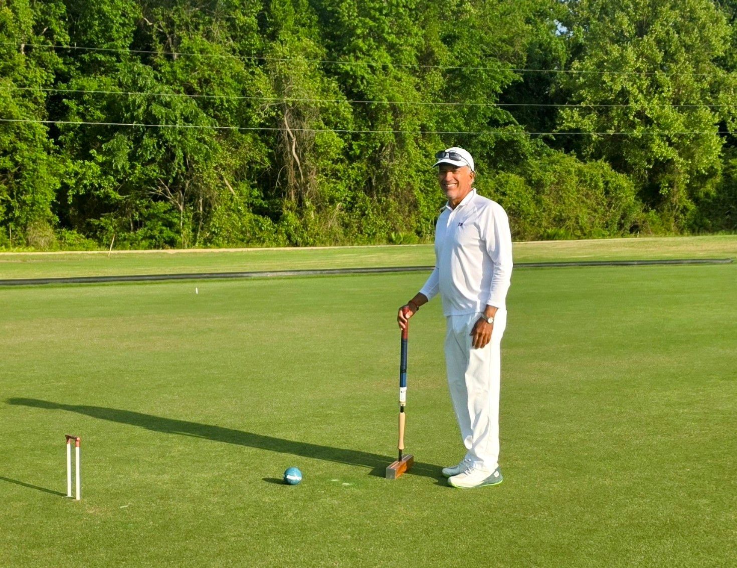 Man in white outfit holding mallet on croquet lawn.