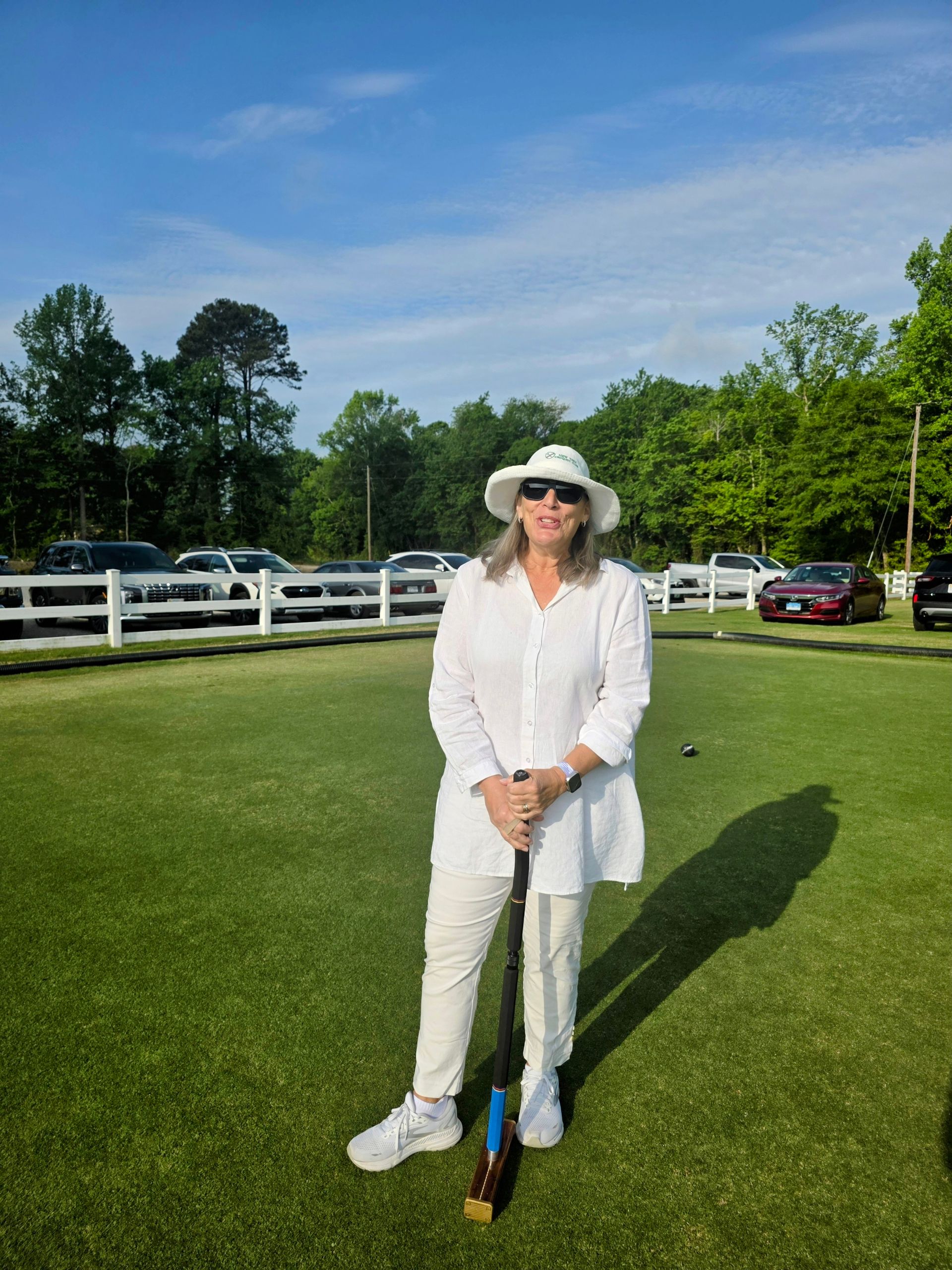 Woman in white outfit and hat holding mallet on a croquet lawn.