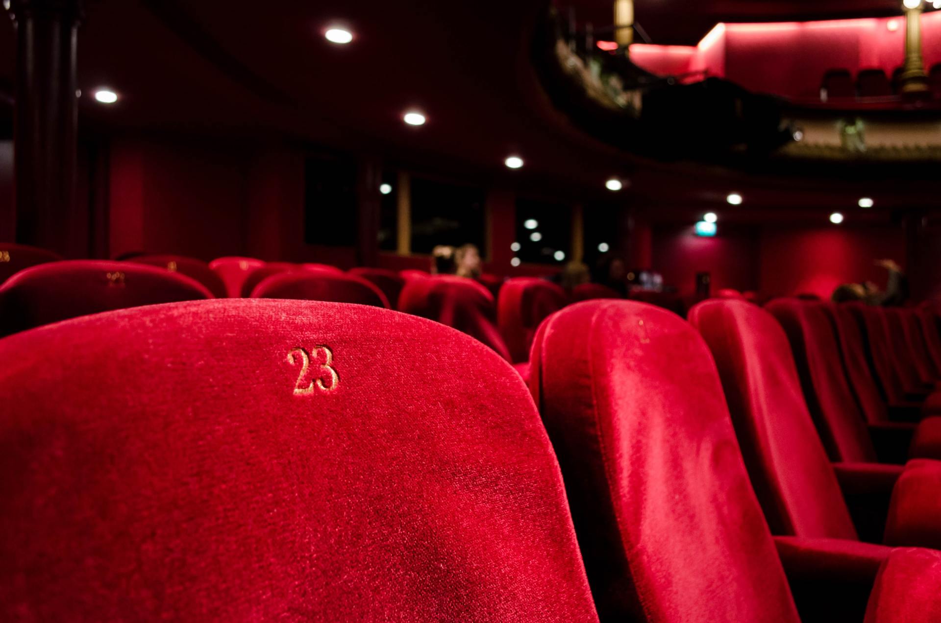 Red velvet theater seats in an empty auditorium. Seat 23 is visible.