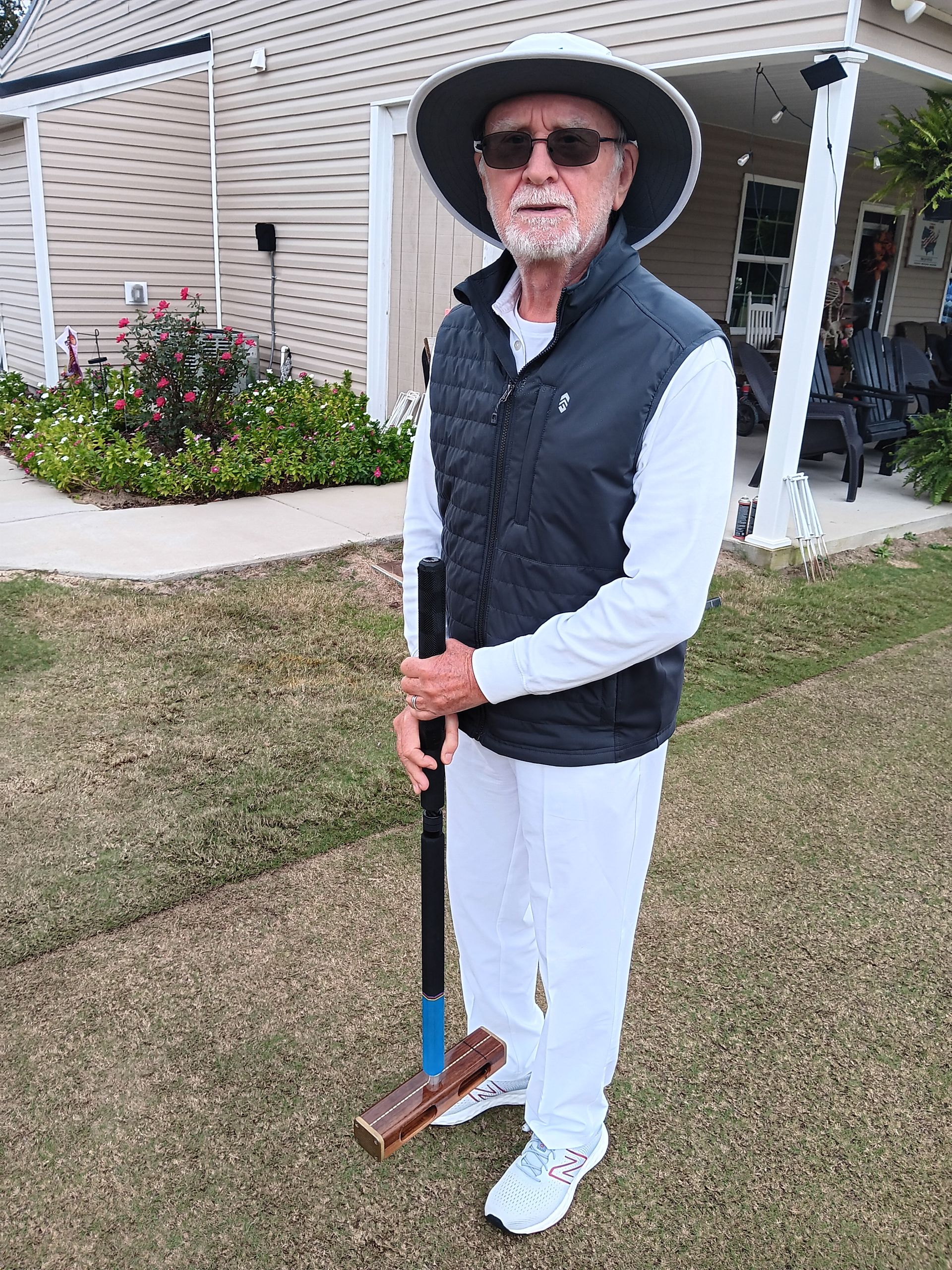 Man in hat and vest holding a croquet mallet on a lawn.