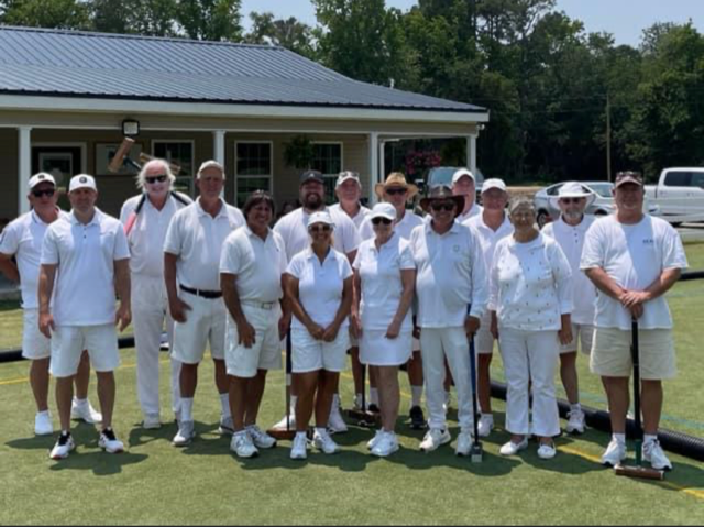 Group of people in white attire, standing on a green lawn near a building.